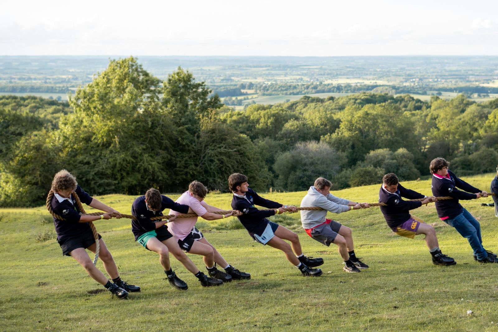 A team pulls a rope together on a sunny lawn; the rope continues out of frame towards an unseen opponent