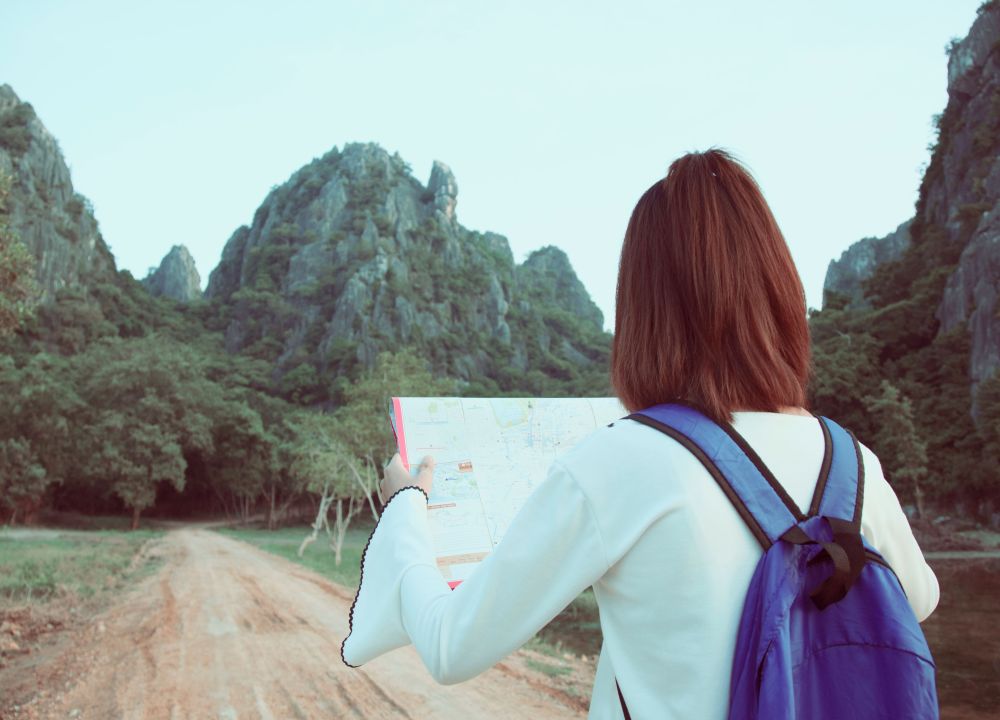 Una viaggiatrice con zaino viola consulta una mappa prima di proseguire lungo un sentiero tra montagne verdi
